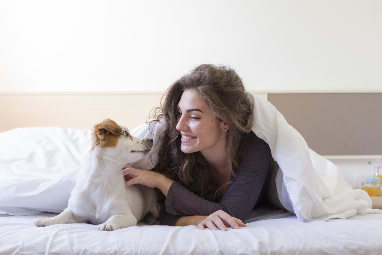 A woman smiling in bed with her dog