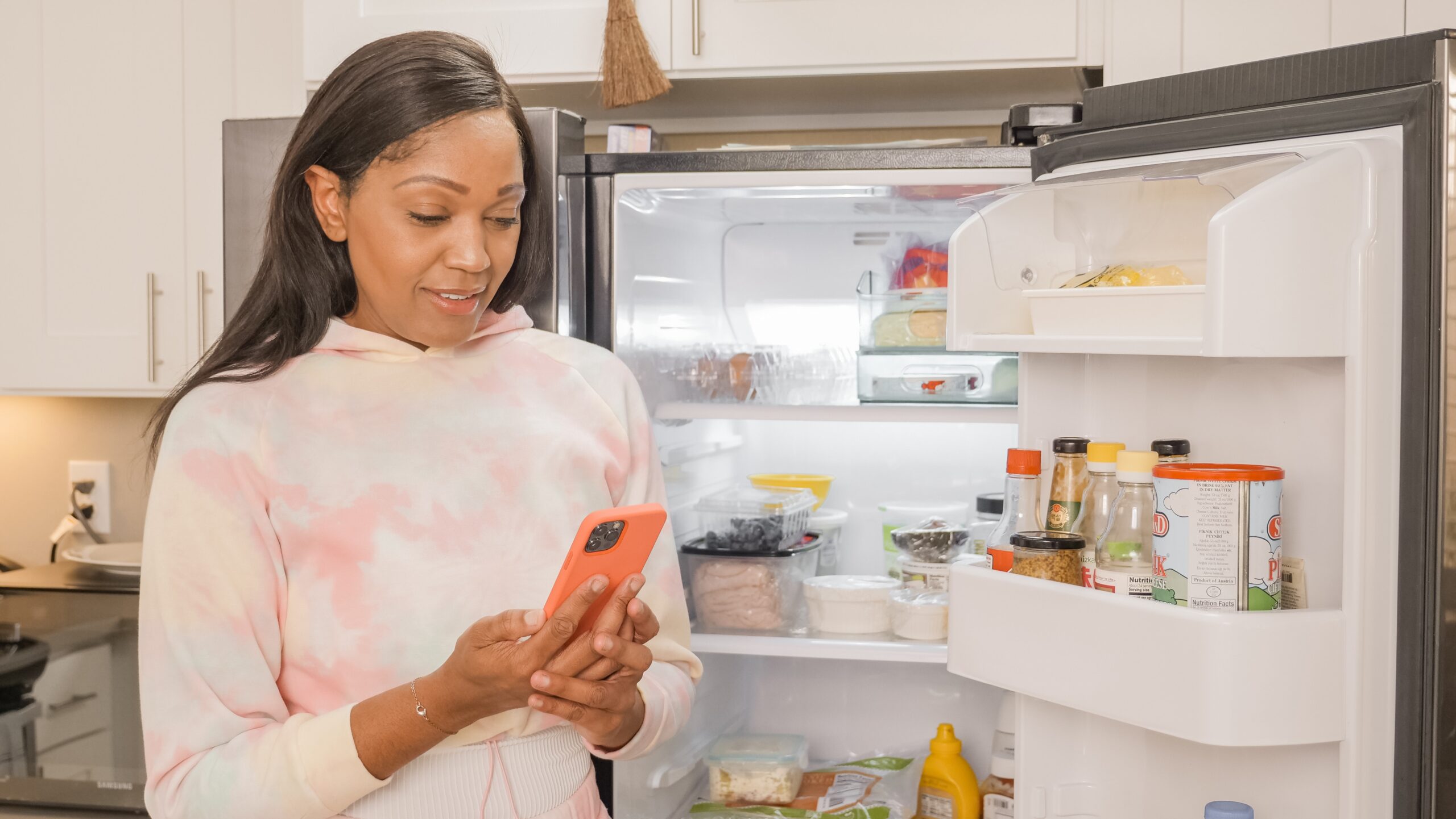 a woman checking her phone beside an open fridge image