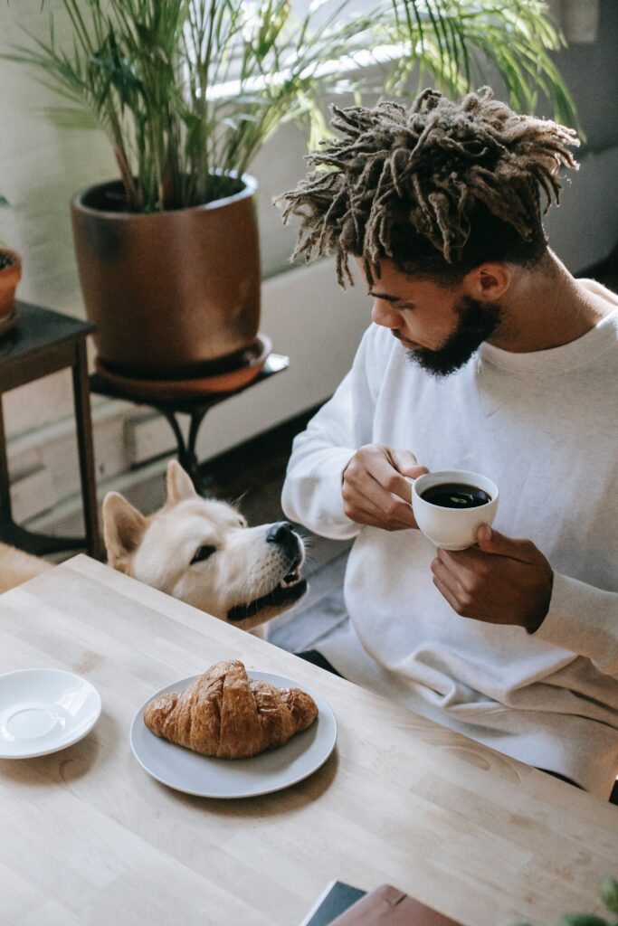 Black man drinking coffee during breakfast and looking at Akita Inu