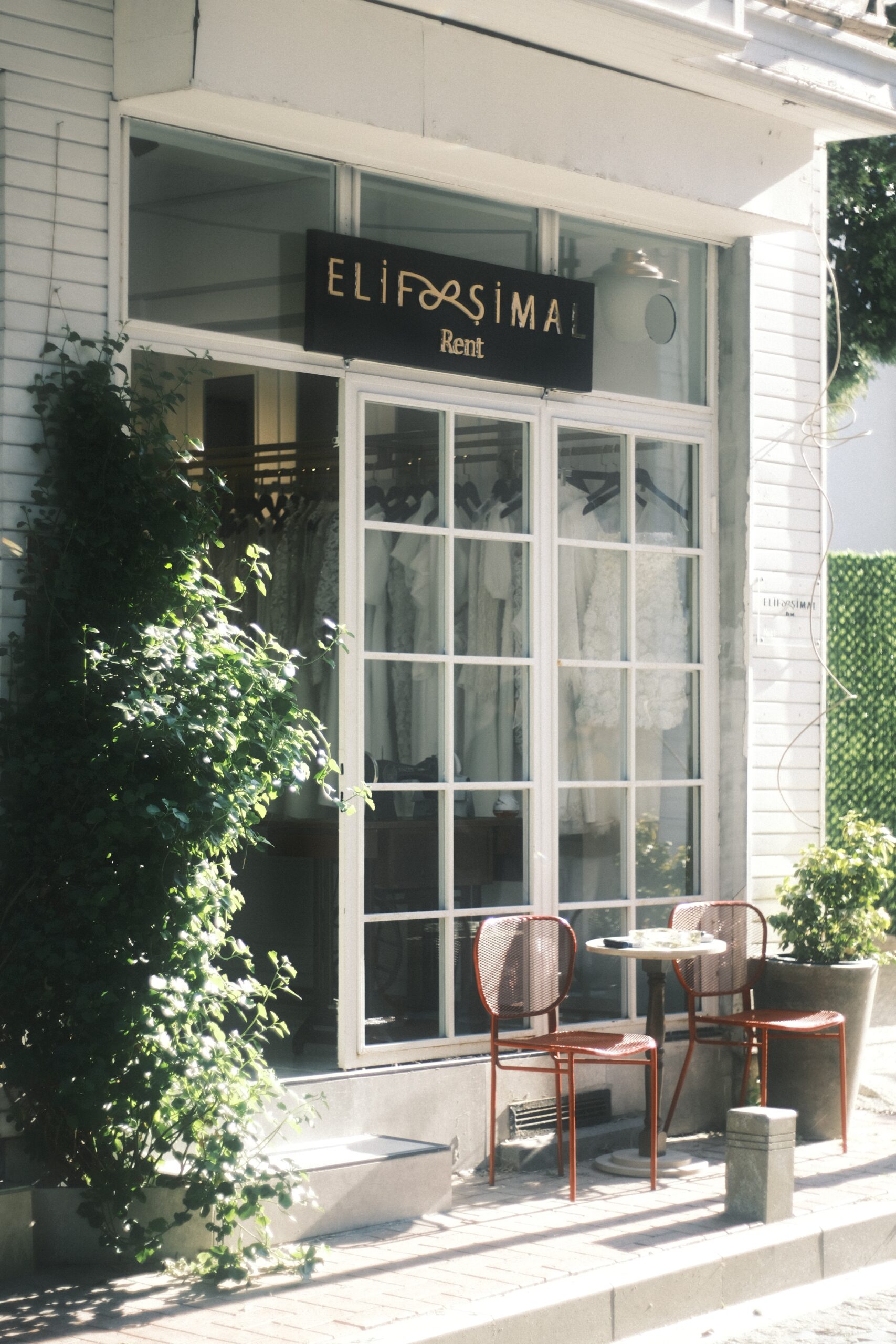 Storefront with table and chairs beside green plants image