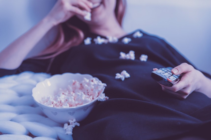 woman holding a remote control while eating popcorn