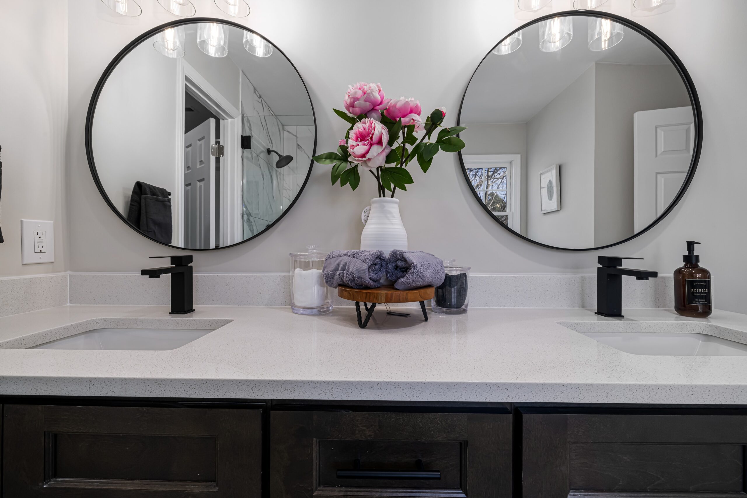A bathroom with round mirrors, white sink and black faucets