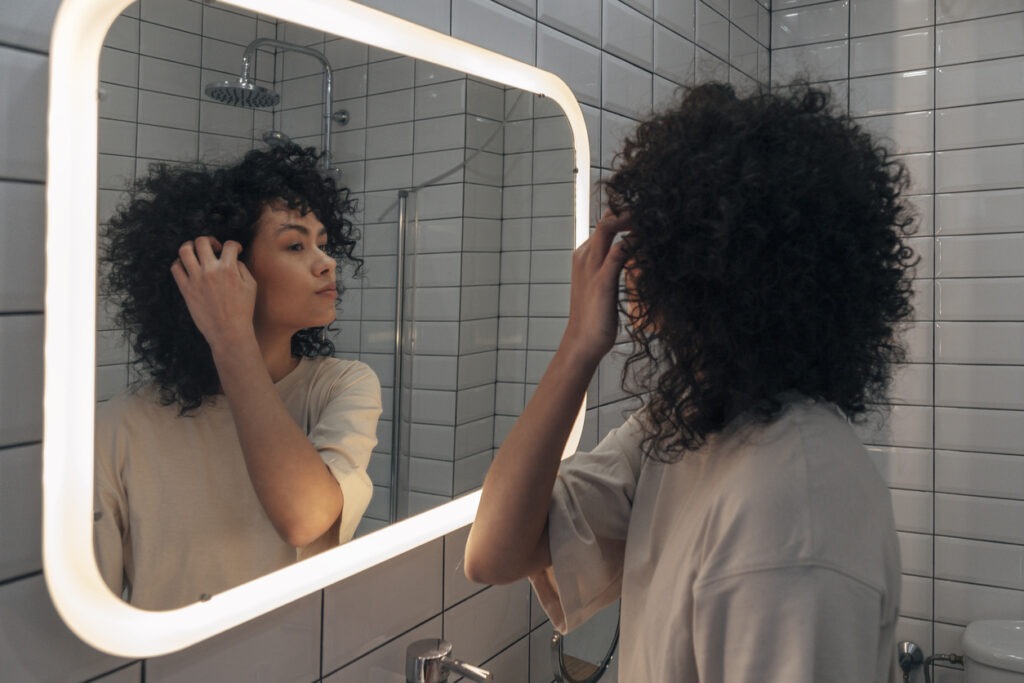 A woman checking herself in a backlit bathroom mirror
