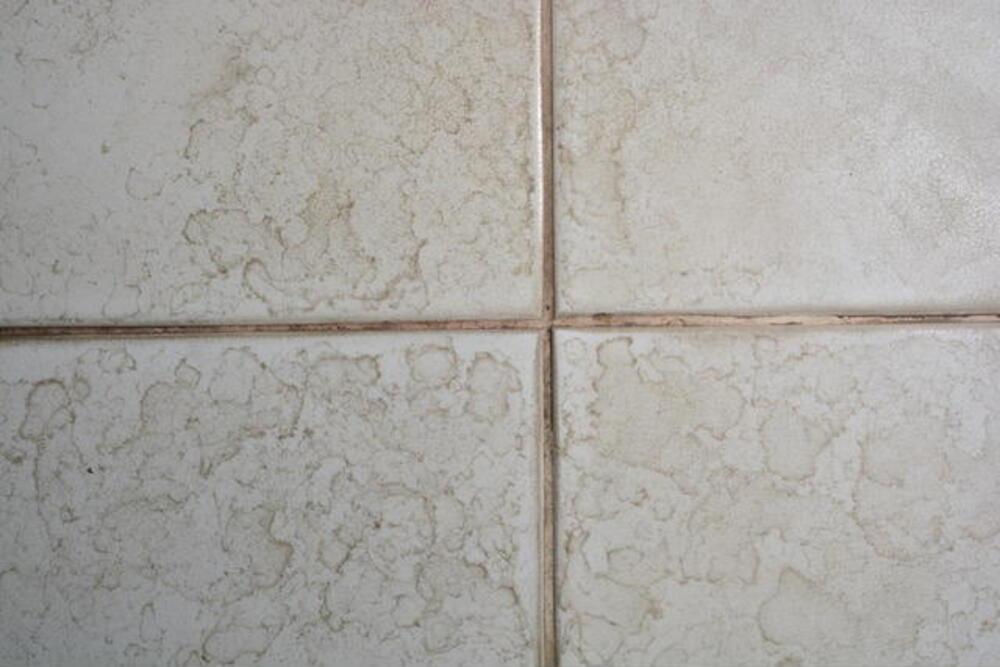How does soap scum develop on bathroom tiles with time