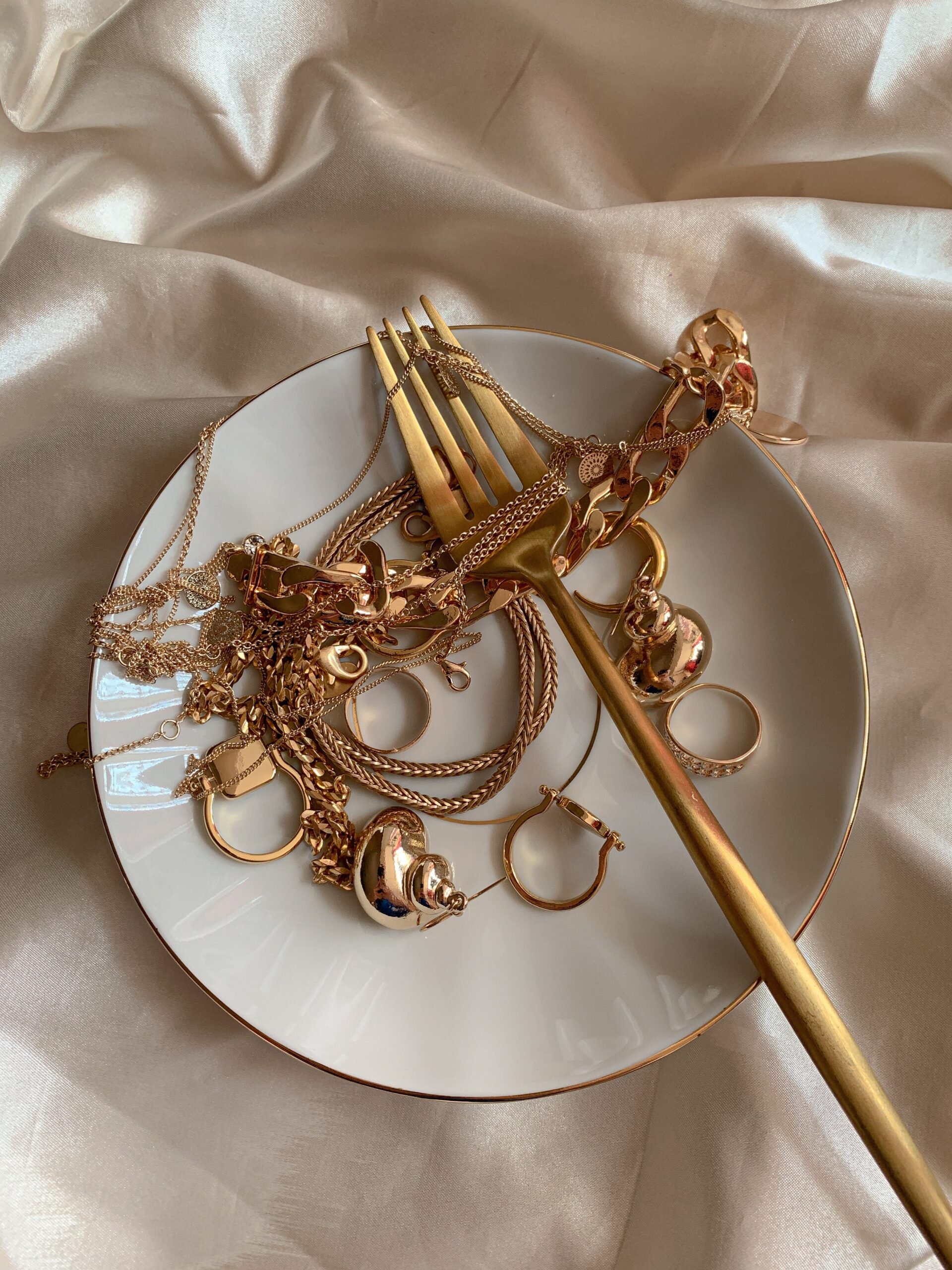 Golden Jewelry and Golden Fork on White Saucer on Beige Silk