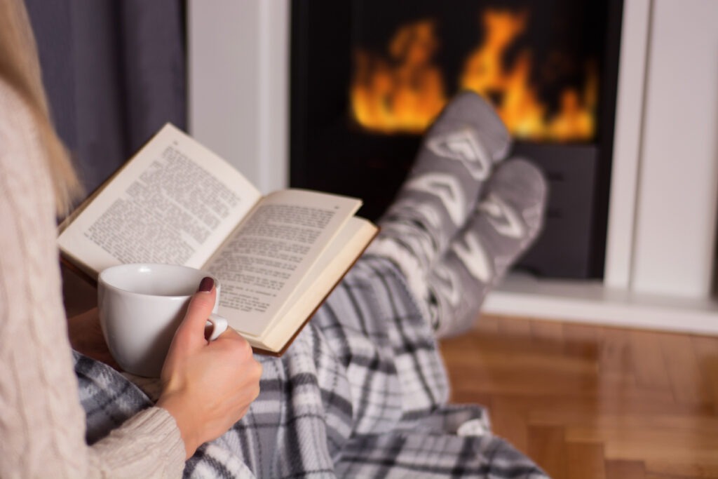 A girl reading a book in front of the fireplace with a plaid blanket
