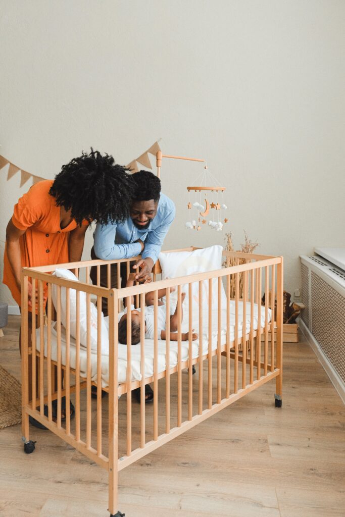 An Image of Parents standing and looking at their baby in a cot