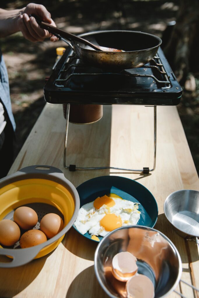 A person cooking eggs on a stove while camping image