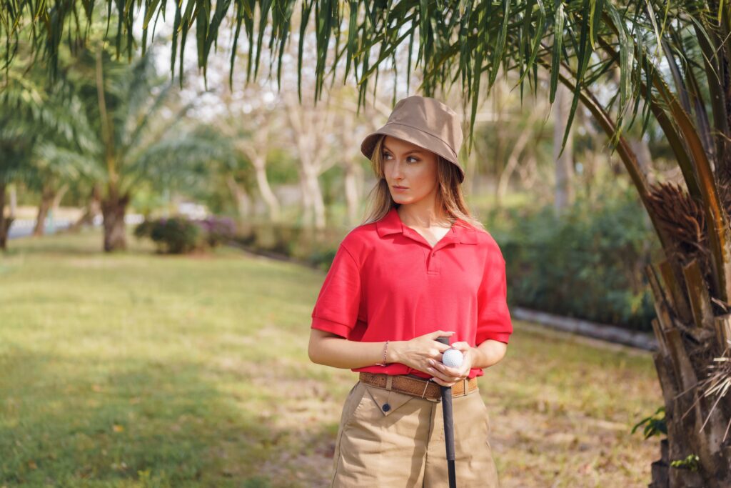 Woman In Pink Polo Shirt And Brown Hat Standing Near Green Grass Field