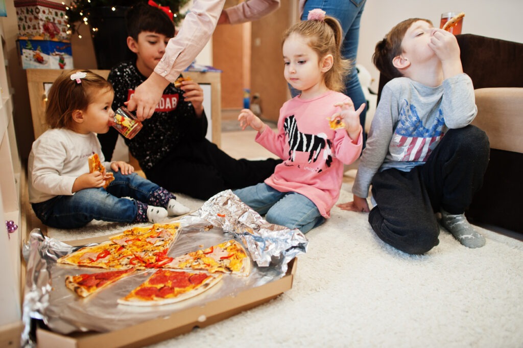 Little children eating pizza on the floor at home
