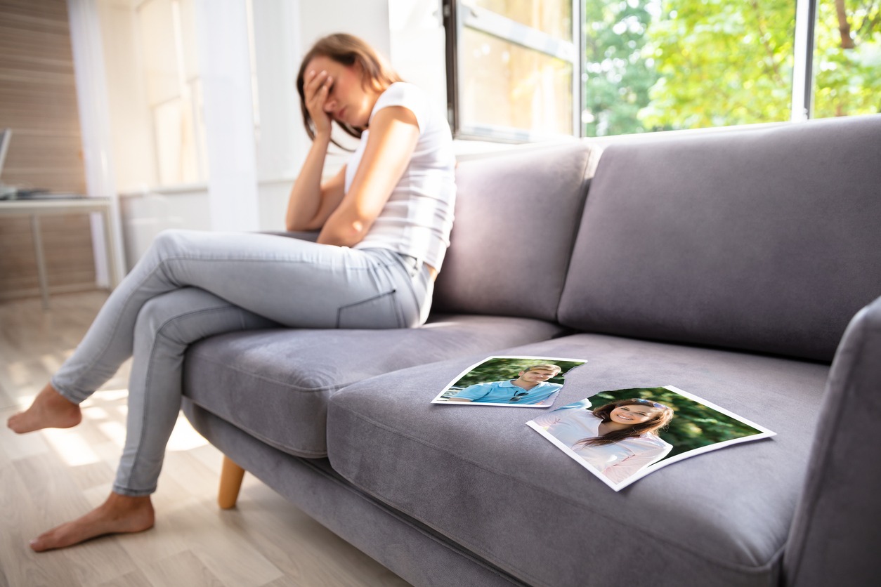 a lonely woman sitting on a sofa with a broken photograph of a couple