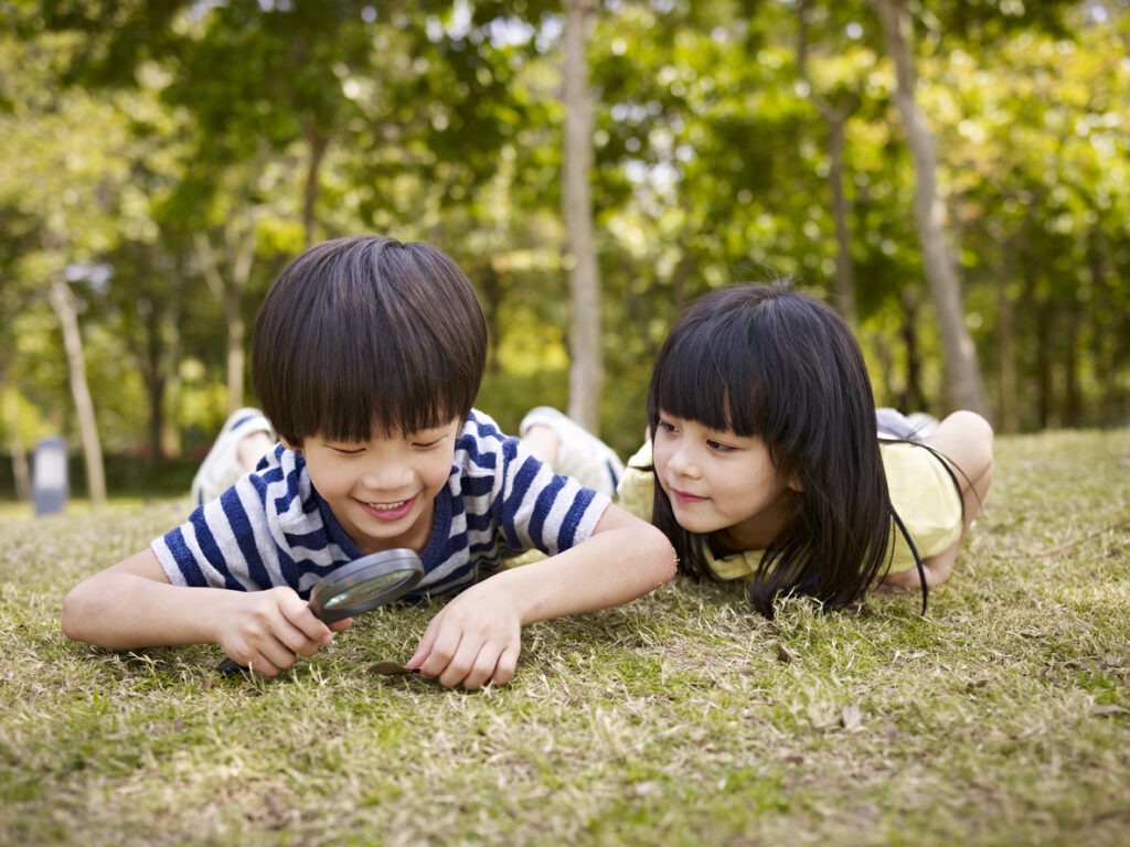 Two kids looking for something in the ground with a magnifier