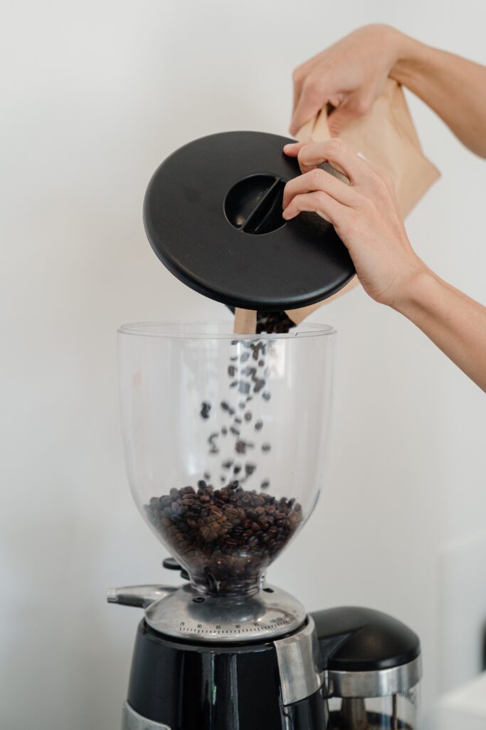 A person pouring roasted coffee beans in a coffee maker image