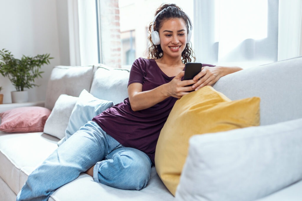 Smiling young woman listening to music with smartphone while sitting on sofa at home
