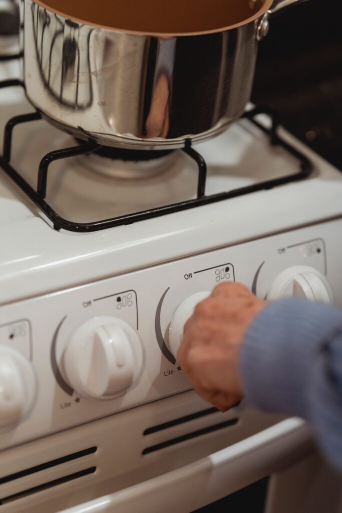  a woman turning the stove knob, with a metal pot image