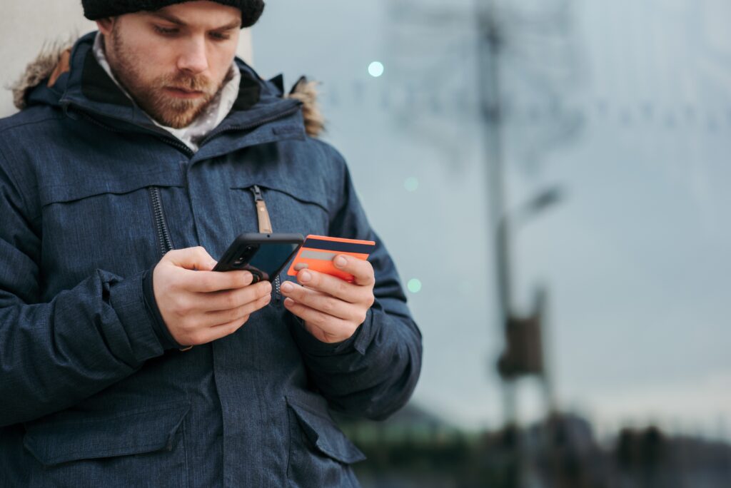 Pensive man holding credit card and browsing smartphone on street in daytime