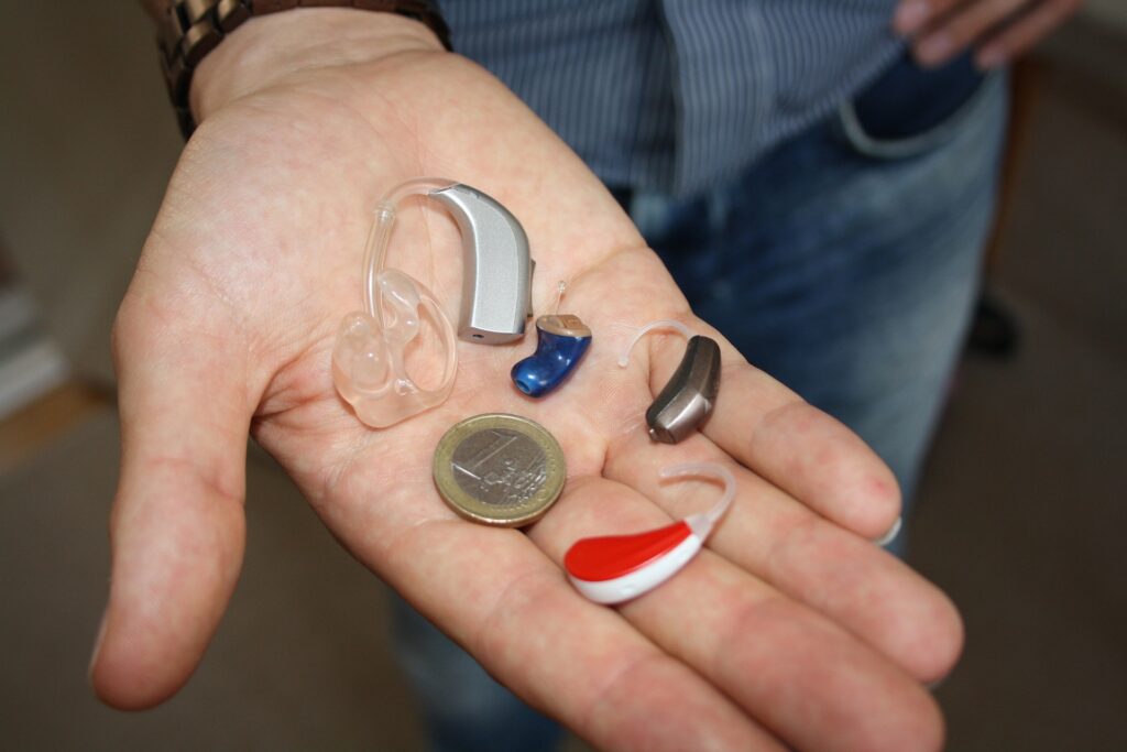 A person holding different kinds of hearing aids in their hands