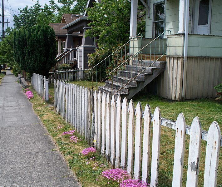 Classic white picket fence next to a sidewalk showing some signs of aging
