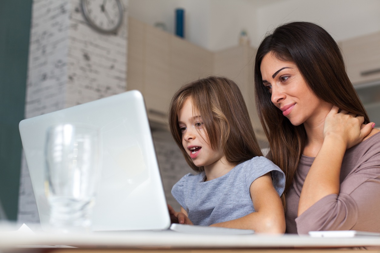 Cute girl and mother using laptop at home