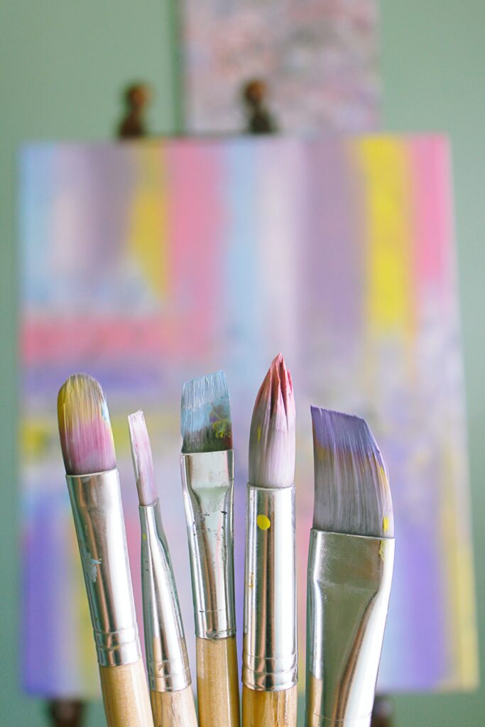 a focused image of paintbrushes in front of a colorful canvas