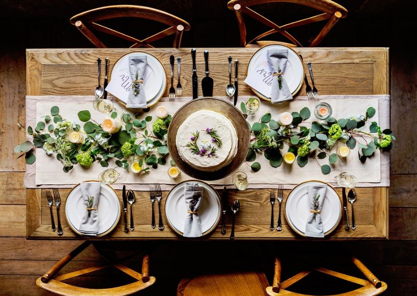 dining table, chairs, formal table setting, utensils, plates, glasses, table napkins, cake, table cloth, candle, leaves, flowers