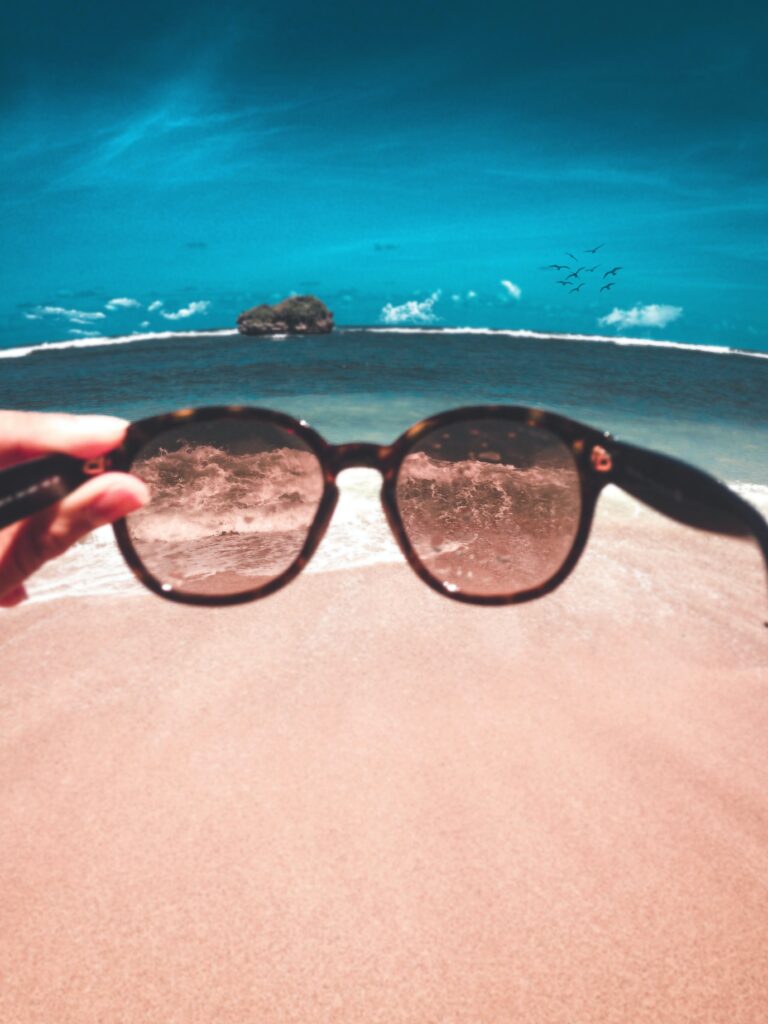 A person holding sunglasses in front of the beach image