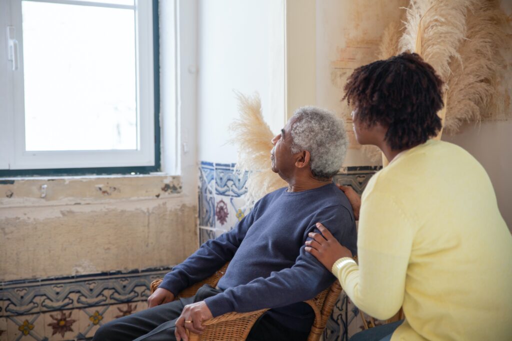 An Image of An elderly man with his caregiver looking at the window