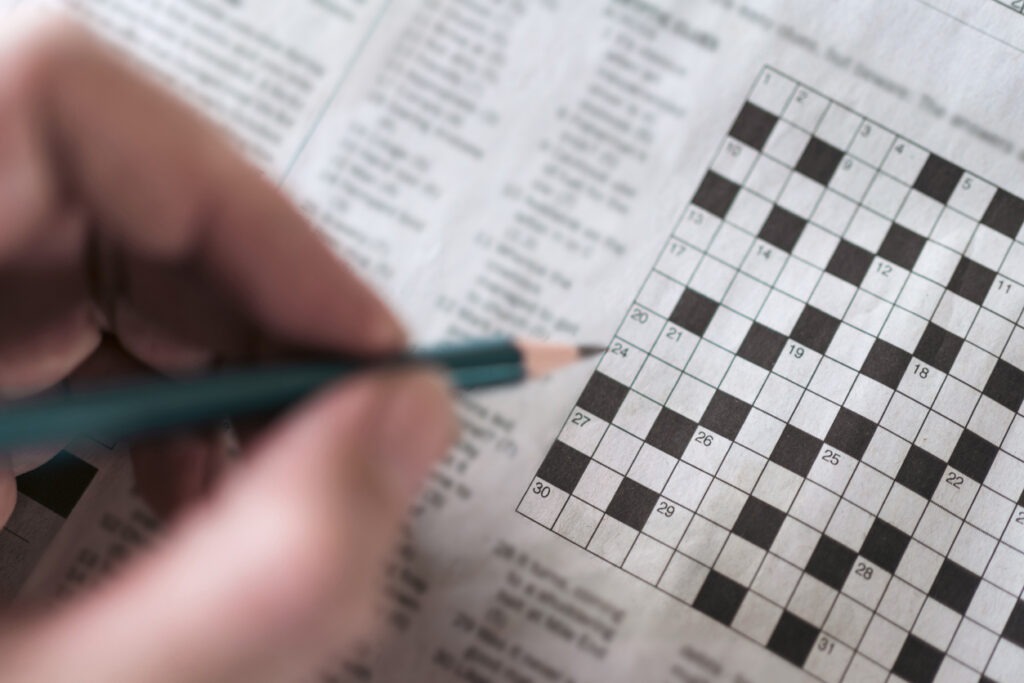 A closeup of hand holding a pencil over a crossword puzzle on a newspaper