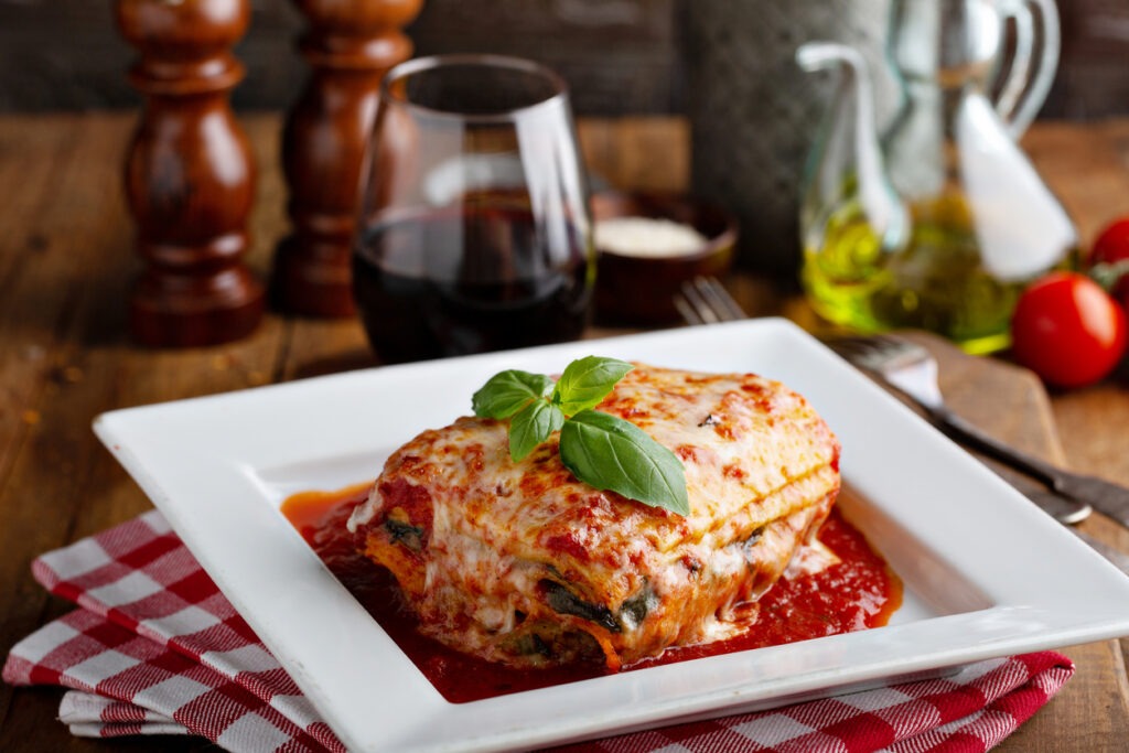 A plate of lasagna besides a glass of wine