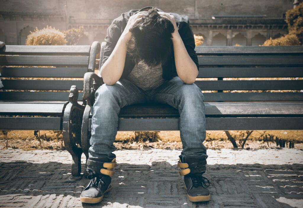 A man sitting on a bench while holding his head image