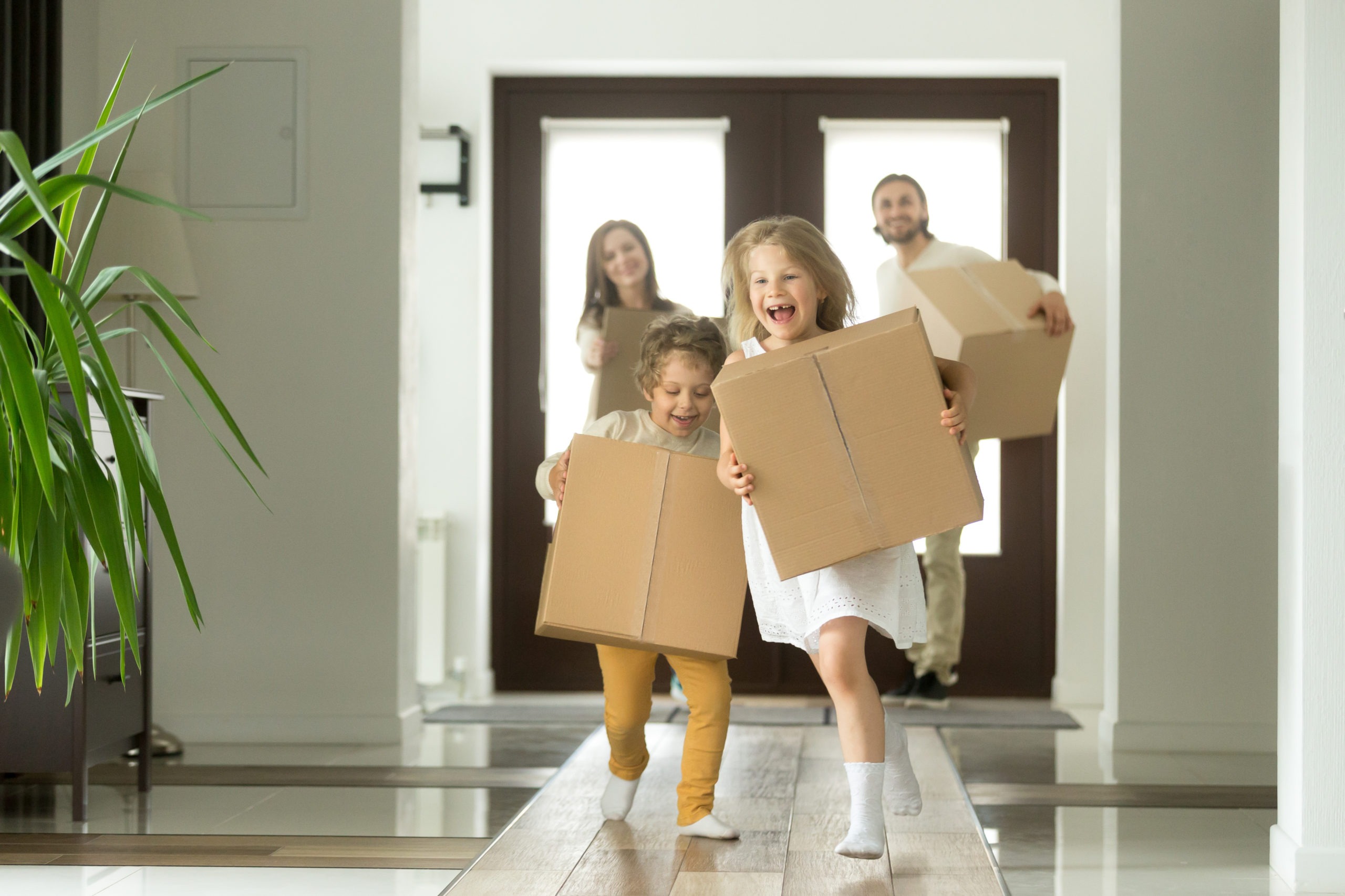 Excited kids running holding boxes, family moving in new house
