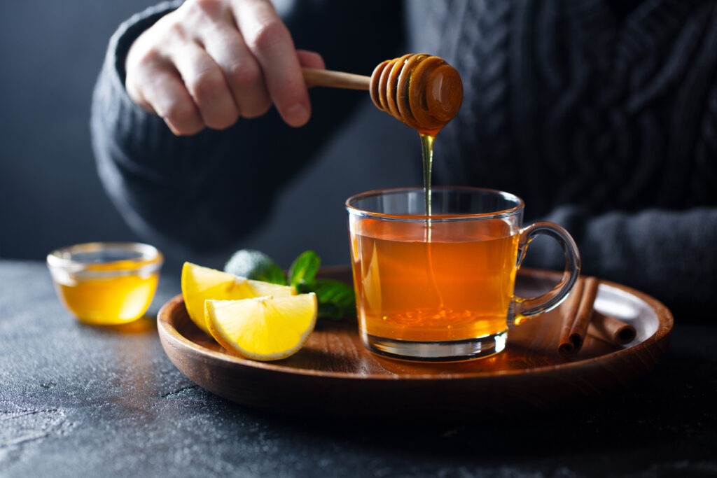 Cup of tea with pouring honey and lemon