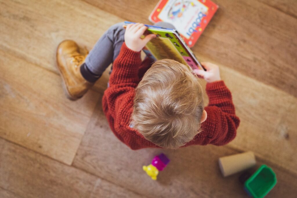 toddler sitting in red sweater holding book