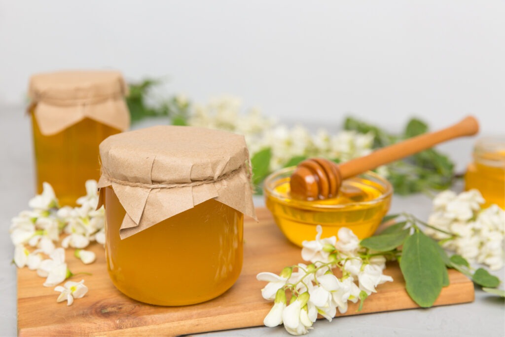 Honey flows from a spoon in a jar. jars of clear fresh acacia honey on wooden background