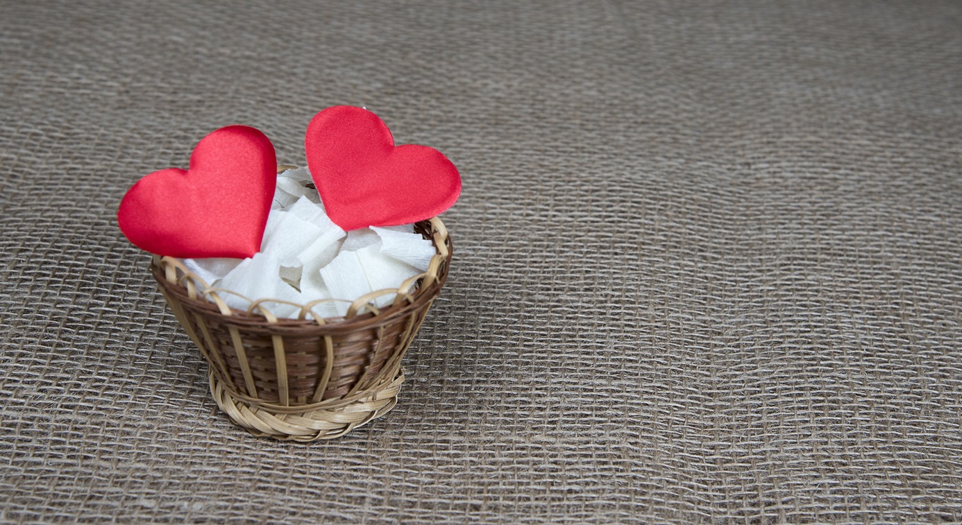 Red hearts in wicker basket on natural burlap background. Valentine day greeting card. Eco concept.