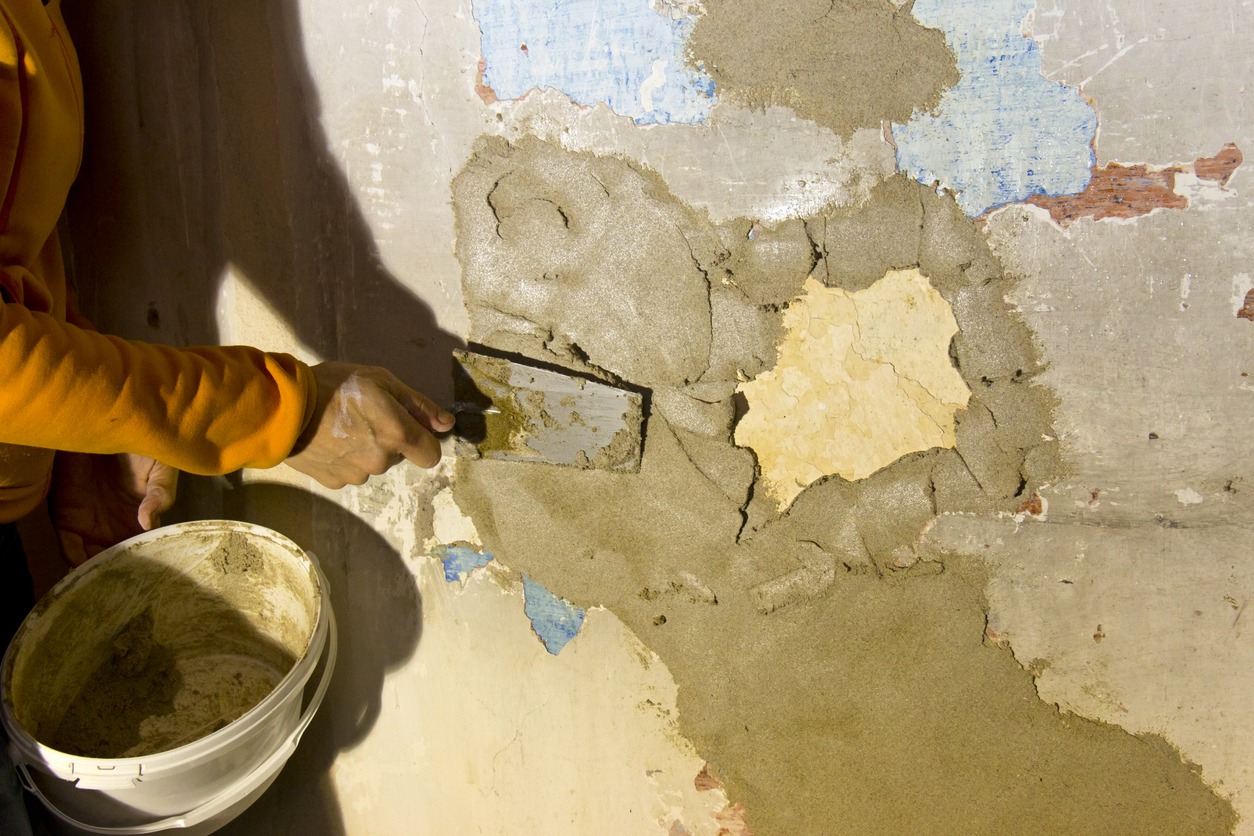 Restorer with plastering tools for restoring a 300 years old wall of a historic farmhouse