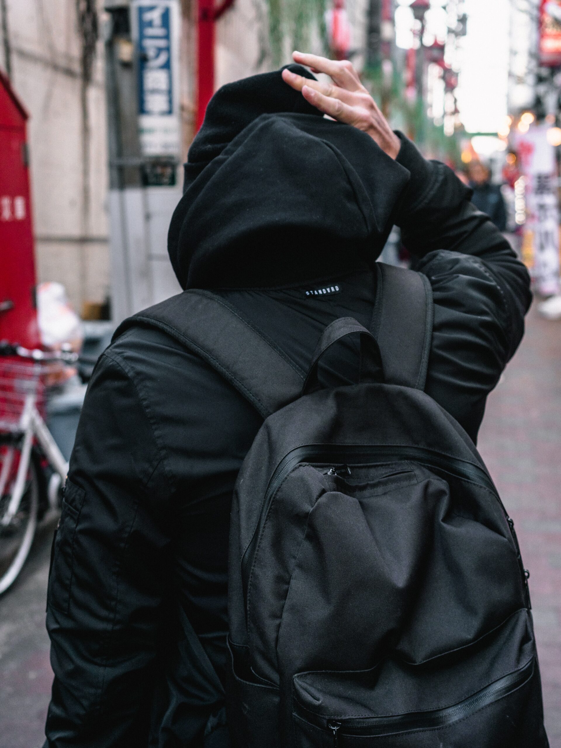 A person wearing a black backpack and walking in a narrow street image