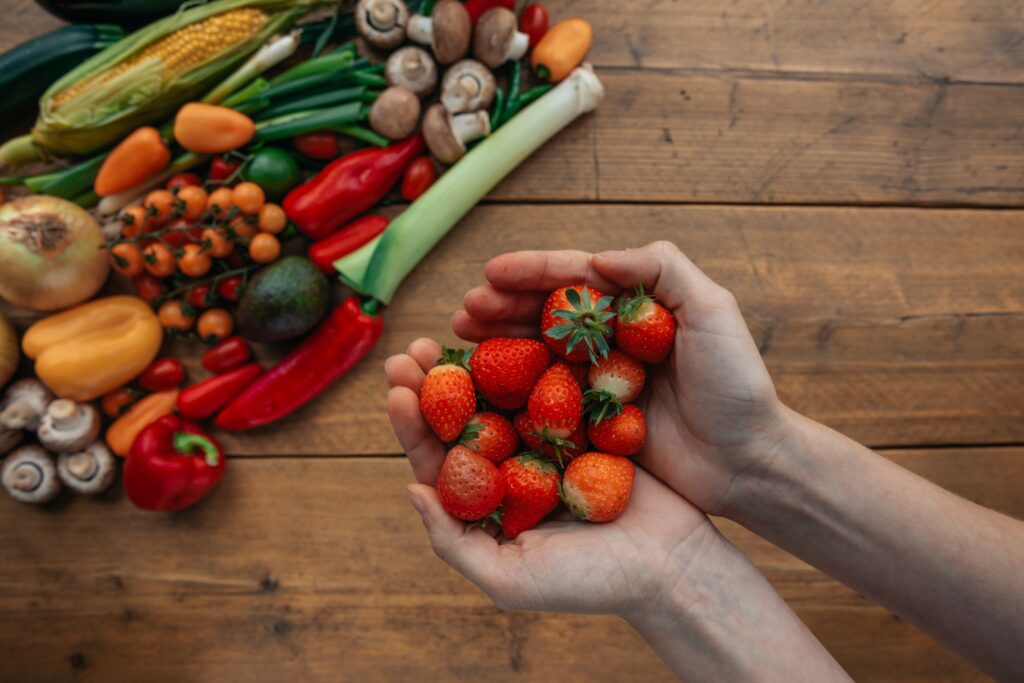 Vegetables on a wooden table and strawberries in hand