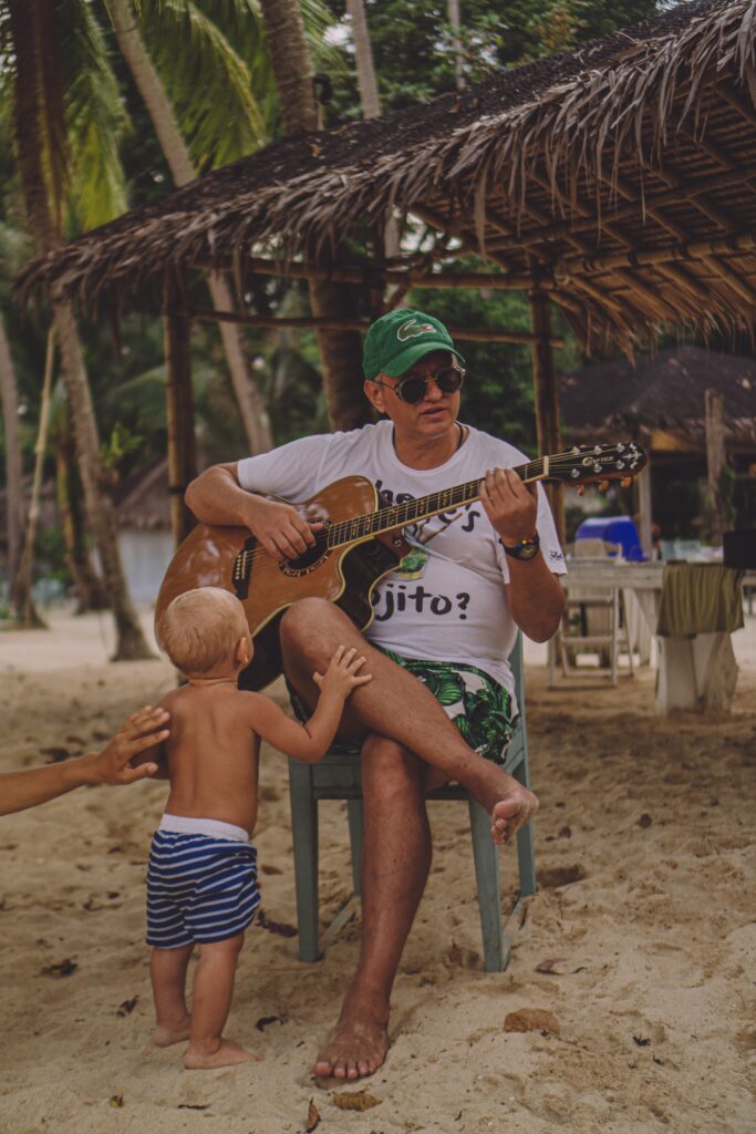 a father playing with his guitar with a toddler wearing a blue-and white beach short image