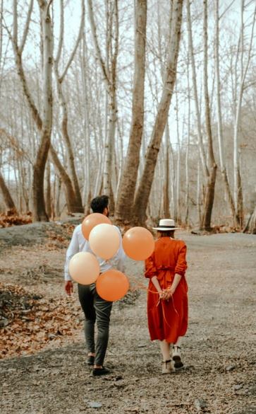 a woman walking with her husband and holding balloons behind her back 
