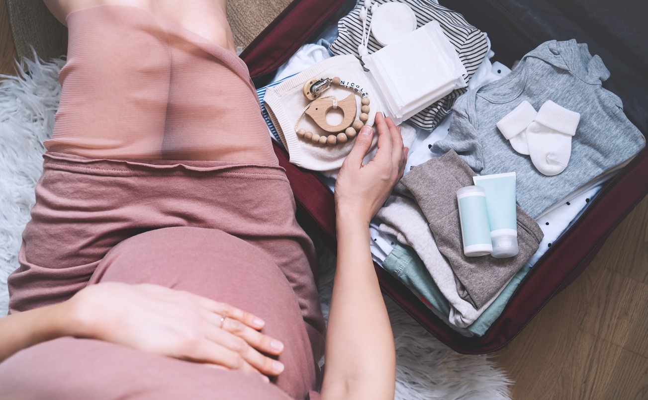 a pregnant woman hugging her belly and packing baby’s stuff