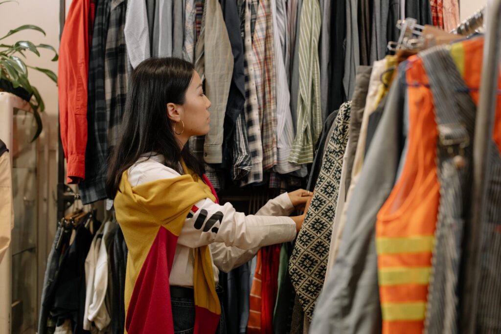 An Image of  A woman wearing white long sleeve choosing clothes in a rack