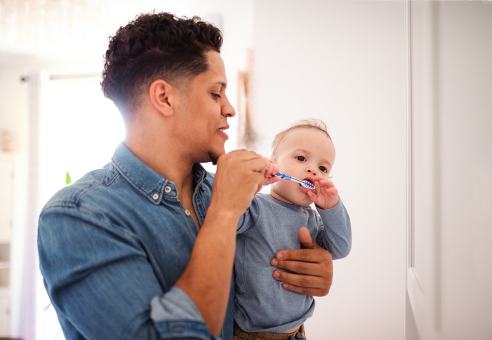 Father and small toddler son in a bathroom indoors at home, brushing teeth.