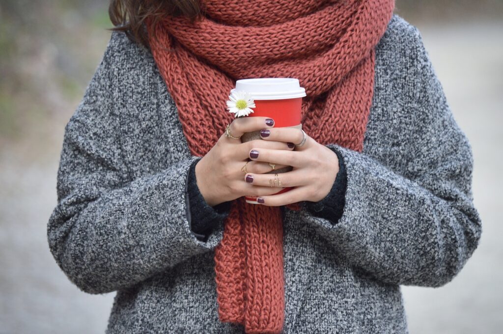 A person with a large scarf holding a coffee cup