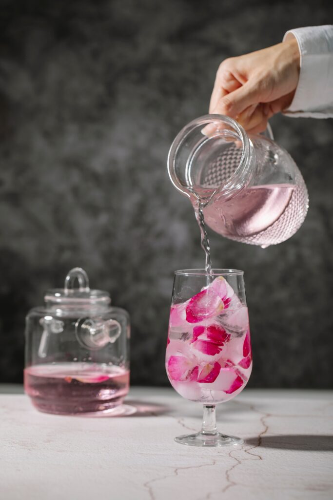 A person pouring water into a glass with ice cubes and rose petals image