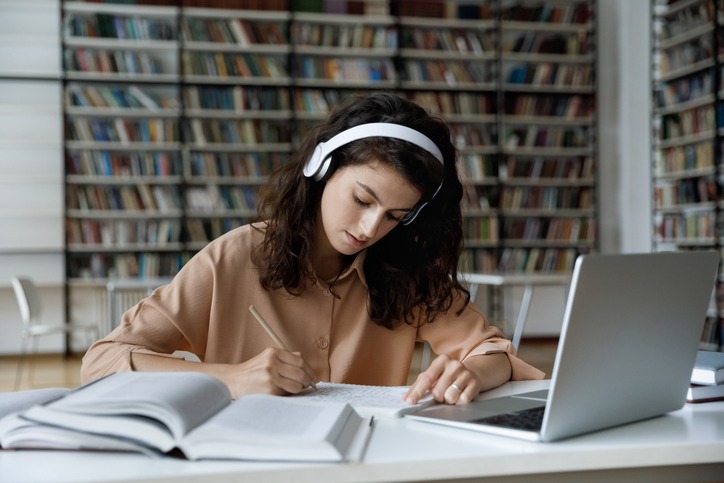 Serious busy hardworking student girl in headphones working essay