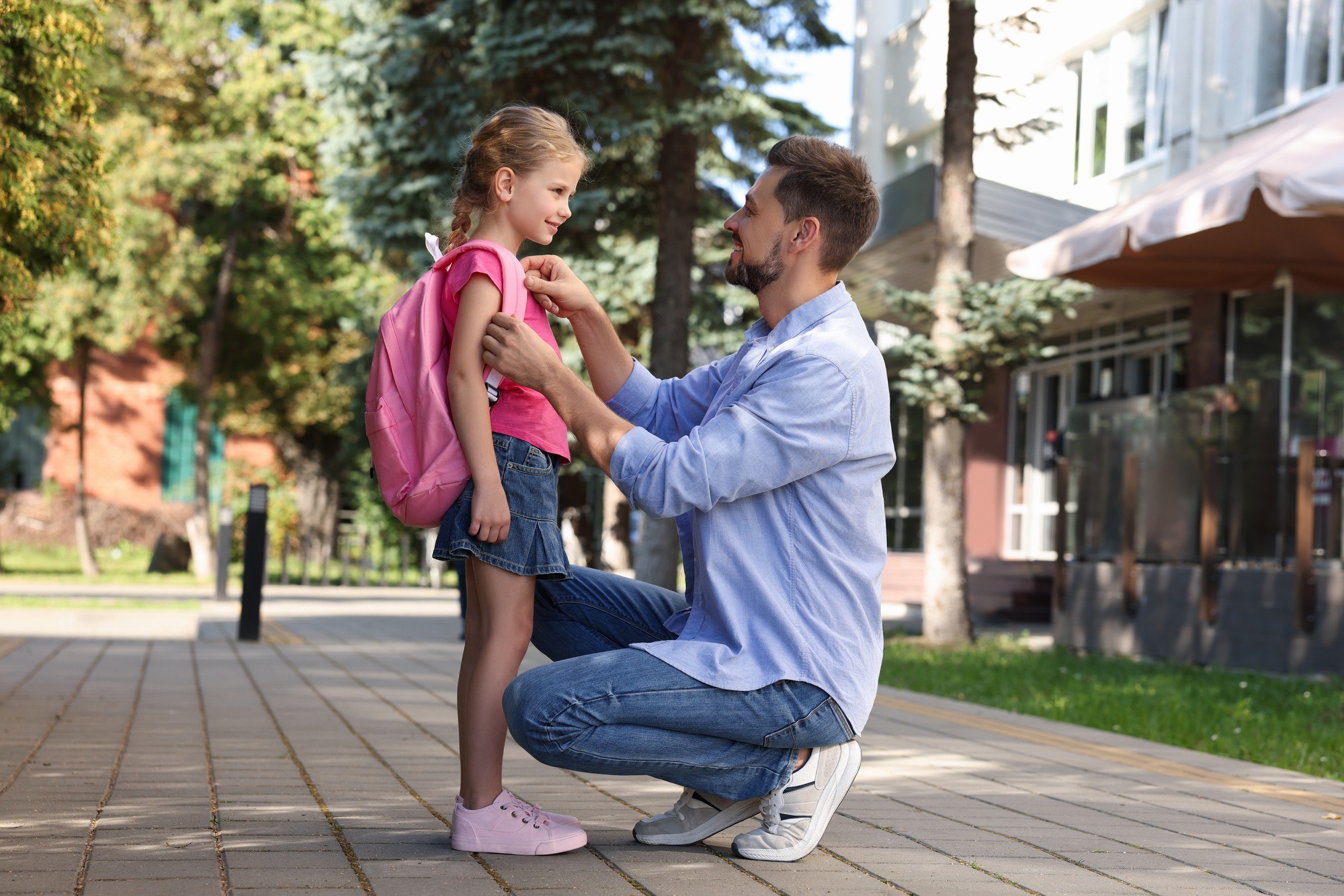 Happy father preparing his daughter to school outdoors