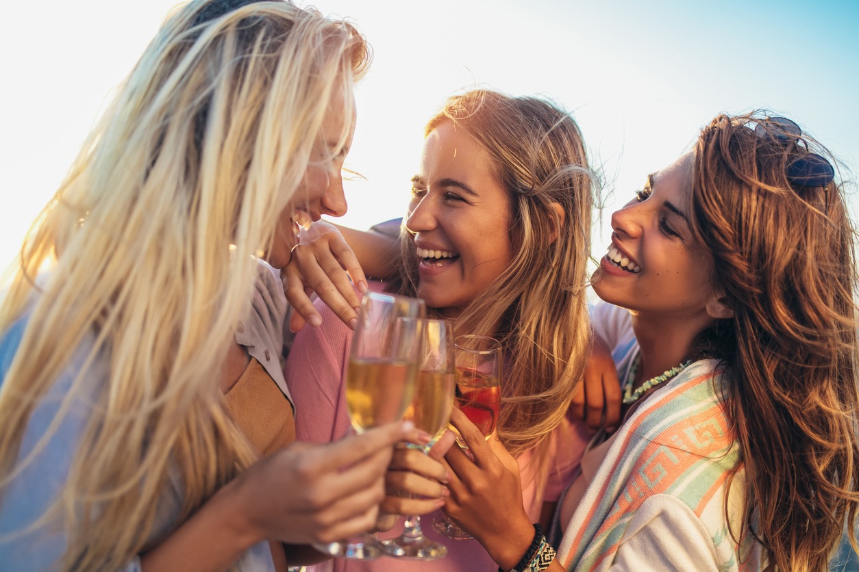 Happy young women drinking champagne at bachelorette party on the beach