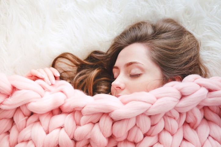 Young woman with long brown hair sleeping under warm knitted peach color throw blanket
