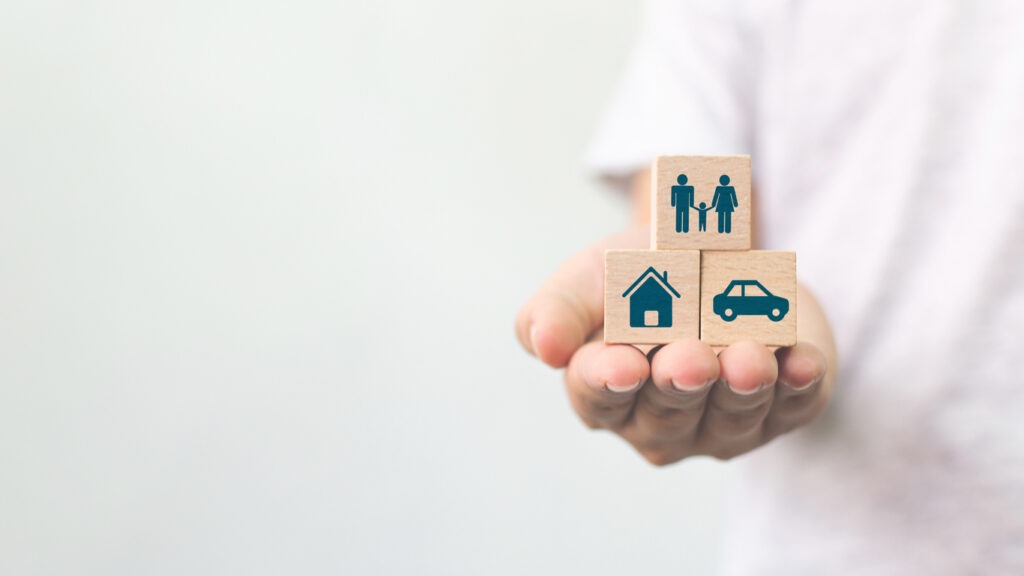 A person holding three blocks illustrating a house, a car and a family